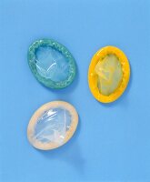 Green, yellow and white coloured condoms on blue background