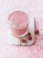 Red creamy smoothie in glass with strawberries on pink designed surface