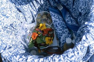 Blick in den Picknickkorb: Schälchen mit Blumensalat, Besteck u. a.