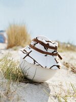 weißer Hut mit braunem Muster auf Volleyball am Strand im Sand