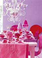 Laid table with red and pink oriental tableware, flowers and candle lanterns