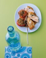 Herby chicken breast with tomato on plate, blurred bottle in foreground
