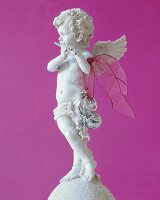 Angel sculpture with flute and key rings against pink background