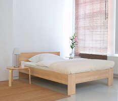 Bed with white linen bed sheet, wooden stool and blinds in bedroom