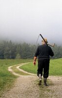 Rear view of man waking with scythe on country lane