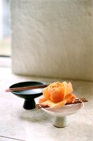 Black and white bowl with chopstick and orange rose on it