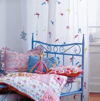 Close-up of blue bed with colourful pillows, blanket and curtains with loops