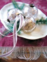 Close-up of white plate with Christmas baubles on purple doilies