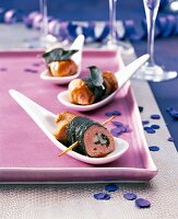 Three tenderloin rolls wrapped in sage leaves on three spoons kept on tray