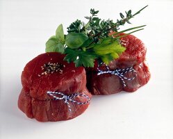 Two raw steaks decorated with herbs on white background