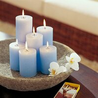 brennende Kerzen in hellblau auf Schale mit Blüten, Streichhölzer