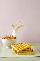 Four saffron kamut waffles with a bowl of tomato salad