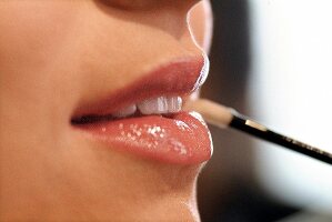 Close-up of woman's lips applying pink lip gloss