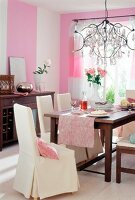 Pink painted room with white chairs, dining table and chandelier