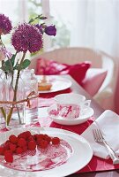 Close-up auf gedeckten Tisch mit Himbeeren + rosa Geschirr