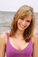 Portrait of beautiful woman wearing purple top standing on beach, smiling