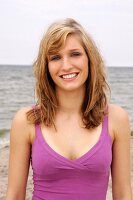 Portrait of beautiful woman wearing purple top standing on beach, smiling