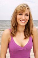 Portrait of beautiful blonde woman wearing pink top standing on beach, smiling