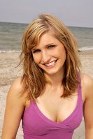 Portrait of beautiful blonde woman wearing pink top standing on beach, smiling