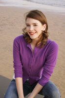 Portrait of beautiful woman wearing purple sweater and jeans sitting on beach, smiling