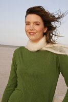 Beautiful woman wearing green sweater, jeans and scarf, standing and smiling