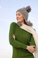 Beautiful woman wearing green sweater, jeans and scarf standing with arms crossed, smiling