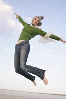 Beautiful woman wearing green sweater, jeans and cap jumping in air, smiling widely