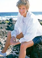Portrait of pretty woman wearing white jacket, shorts and canvas shoes sitting, smiling