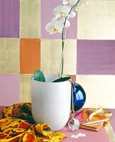 White glass vase with flower, scarf, magnifying glass, belt and pen against colourful wall