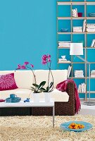 Living room with wicker sofa, white cushions and bookcase against blue wall