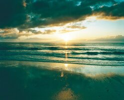 Meeresstrand beim Sonnenuntergang: Sand, Wellen, Himmel bewölkt