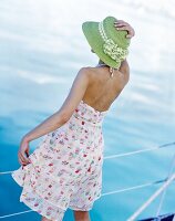 Rear view of woman wearing green hat and summer dress standing against railing