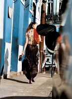 Woman wearing polka dots top walking on street while carrying mesh bag on shoulder