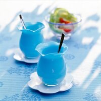 Two blue glasses with spoon and wavy rim on white saucer