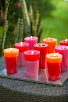 Kerzen in zwei verschiedenen Farben stehen auf einem Tablett im Garten.x