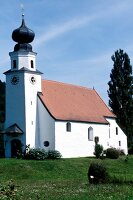 Kleine, weiße Kirche mit einem Zwiebelturm auf einer Wiese.