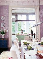 Dining table decorated with candlesticks and artichokes in front of modern kitchen