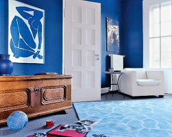 Wohnzimmer mit blauen Wänden, Sessel und rustikalen Holztruhe.