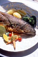 Fisch ganz + Kartoffeln, Möhren, Brokkoli auf Teller in Weiß