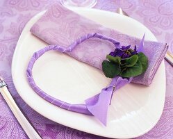 Ribbon in the form of heart decorated with bunch of small violets and napkin on plate
