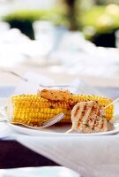 Corn cob with chicken and apple skewers on plate