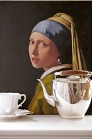 Silver plated teapot and cup in front of oil painting