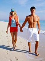 Happy couple walking hand in hand on  beach, smiling