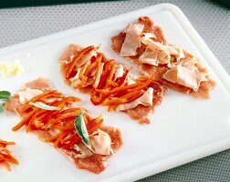 Close-up of schnitzel topped with mortadella stripes and red pepper strips on white board
