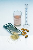 Almonds, steel grater and rose water in measuring glass and tube on white background