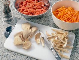 Mushrooms cut in thin strips on cutting board, carrot strips and beef strips in bowls