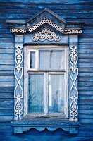 Typisches, verziertes Fenster an einem blauen Holzhaus in Russland