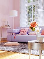 Lilac sofa and silver-leaf side table in living room with pink walls