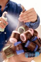 Curling spray being sprayed on woman's hair withy curlers