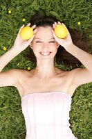 Frau im Gras lacht , hält sich zwei Zitronen an den Kopf